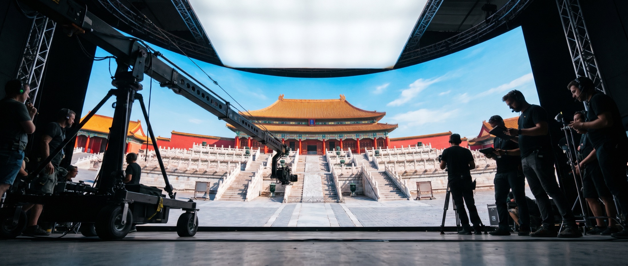 虚拟制片棚概念示意：弧形 LED 幕墙播放宫殿广场外景，前景是摇臂与轨道车，摄制组在两侧待命